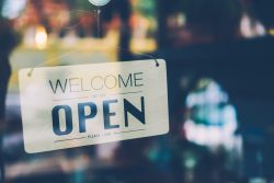 Close up of sign in a store window reading, "Welcome, we are open."