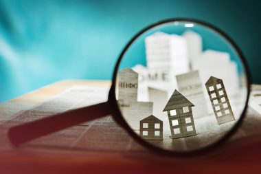 Paper houses and buildings behind a magnifying glass. 