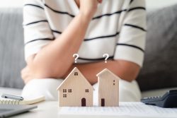 woman is deciding to choose house with Small Wooden House Model with Question Marks, Planning to buy property. Choose what's the best. home loan concepts."n