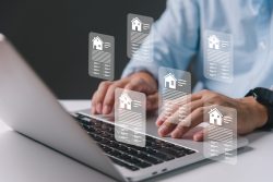 Close up of a person on a laptop conducting a real estate analysis on the keyboard, with images of houses hovering over the keyboard.